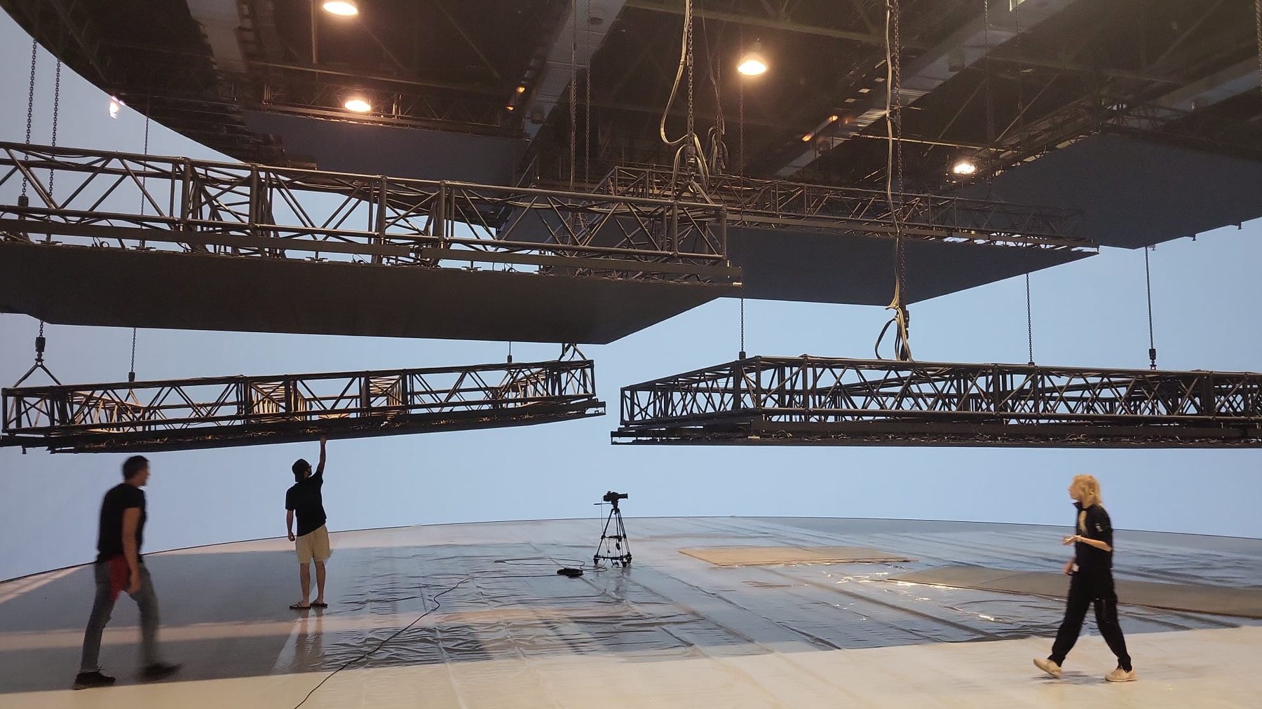 Travi di truss sospese in studio durante il montaggio, con tecnici al lavoro.